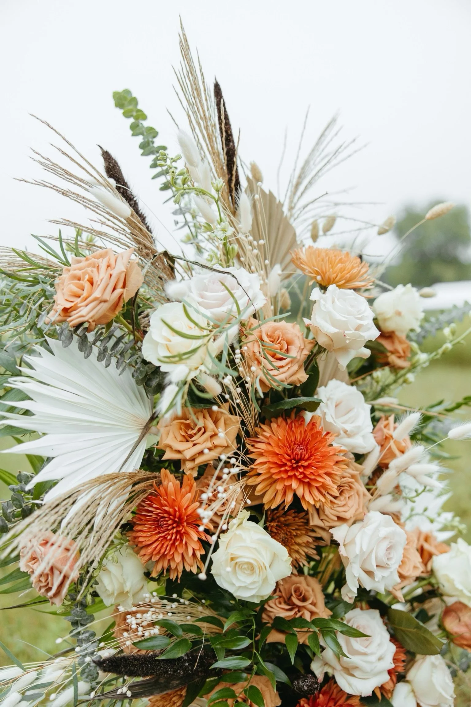 Floral arrangement with orange dahlias, white roses, dried leaves, and greenery.