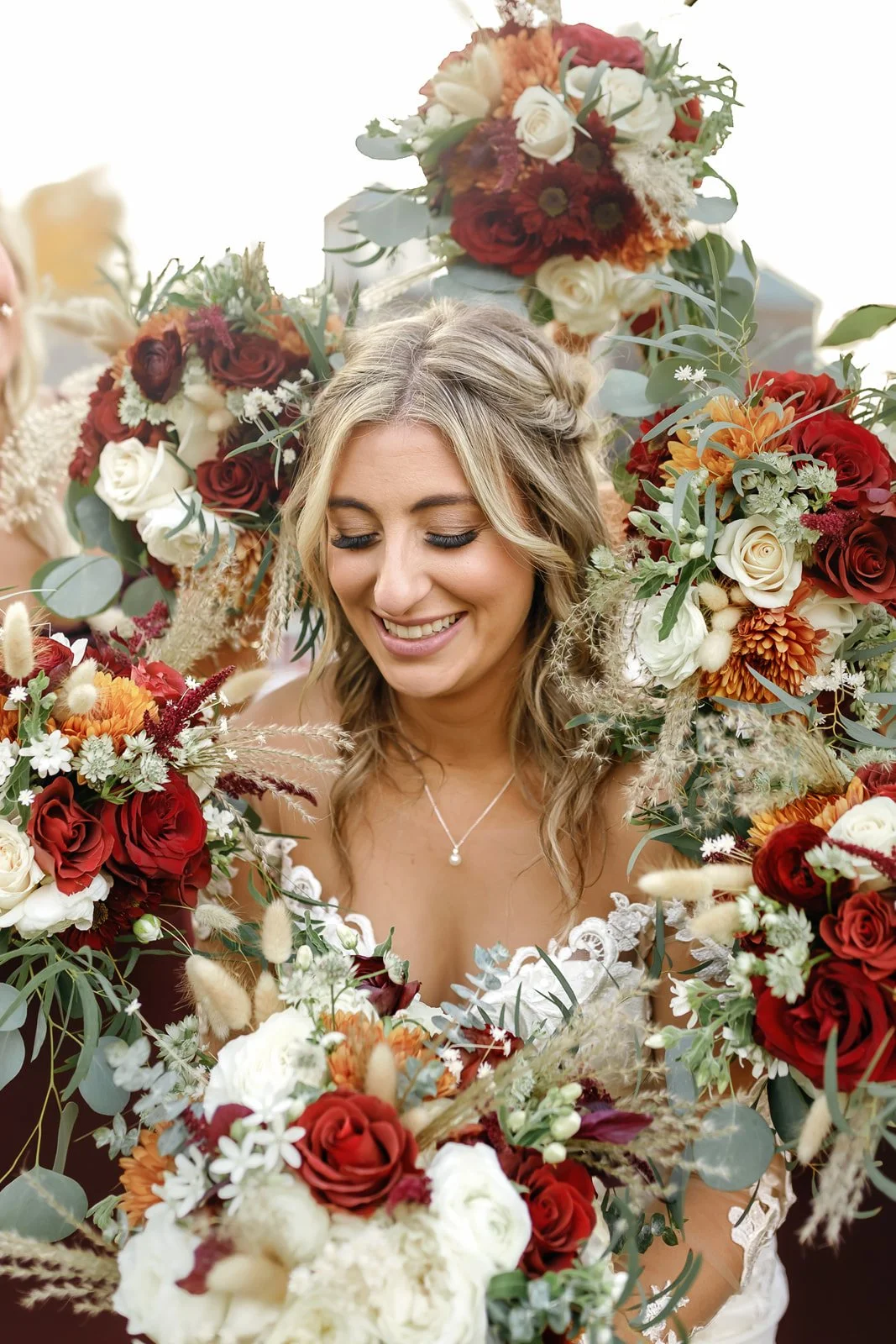 Smiling woman surrounded by bouquets of red, white, and orange flowers with green foliage.