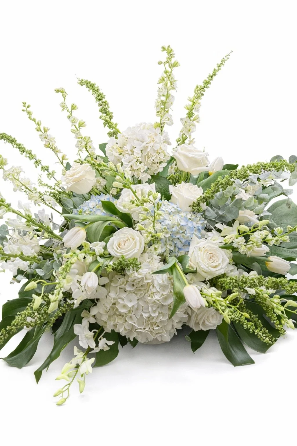 A floral arrangement with white roses, white hydrangeas, tulips, and various green foliage set against a white background.