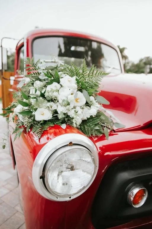 Red vintage truck with white floral arrangement on hood