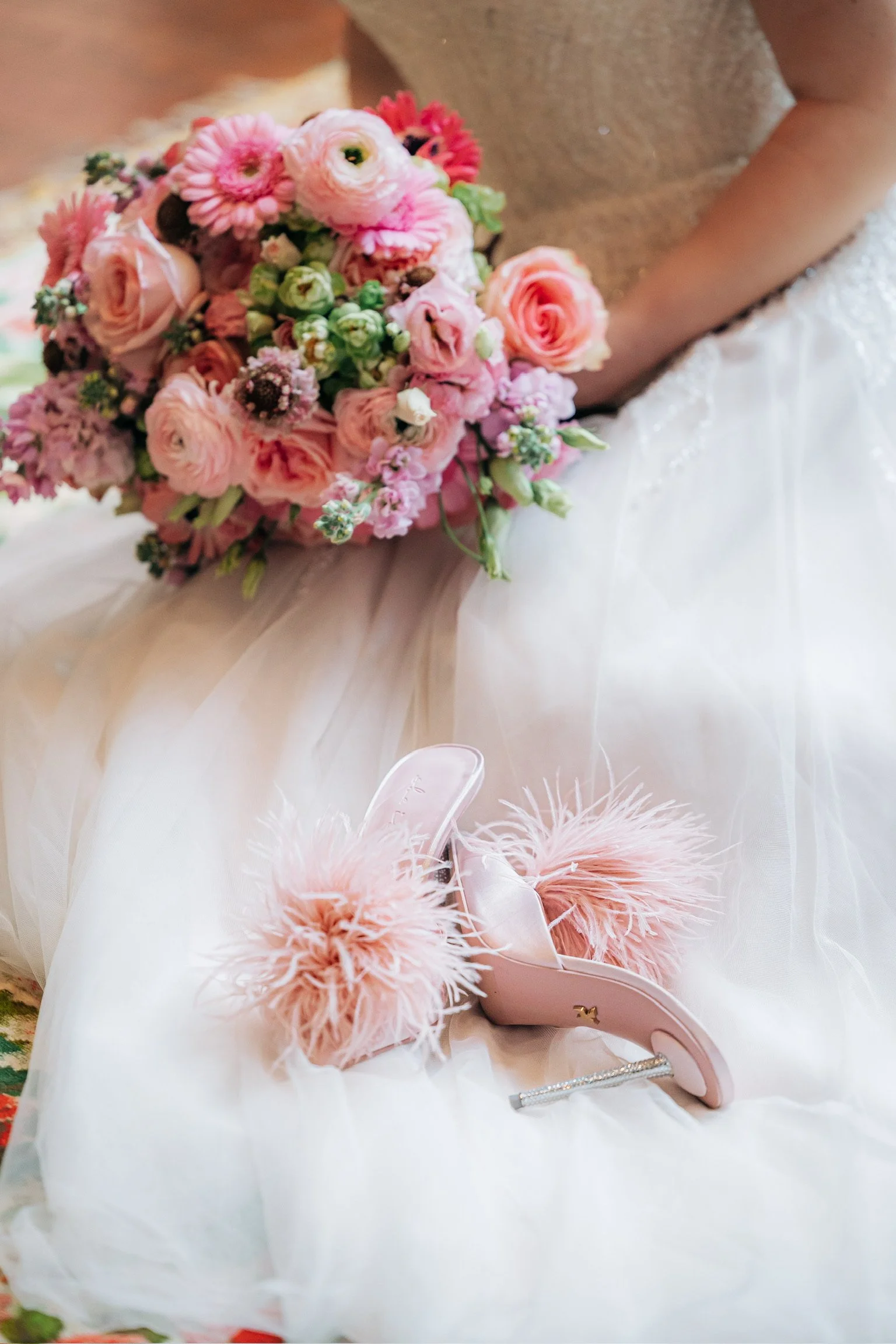Bridal bouquet in shades of pink and peach, with fluffy pink slippers on a wedding dress.