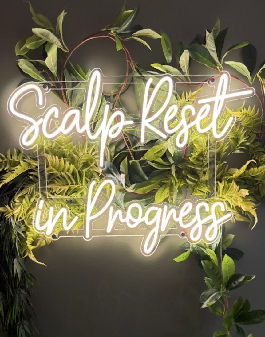 Neon sign reading 'Scaling Reset in Progress' surrounded by green leafy plants.