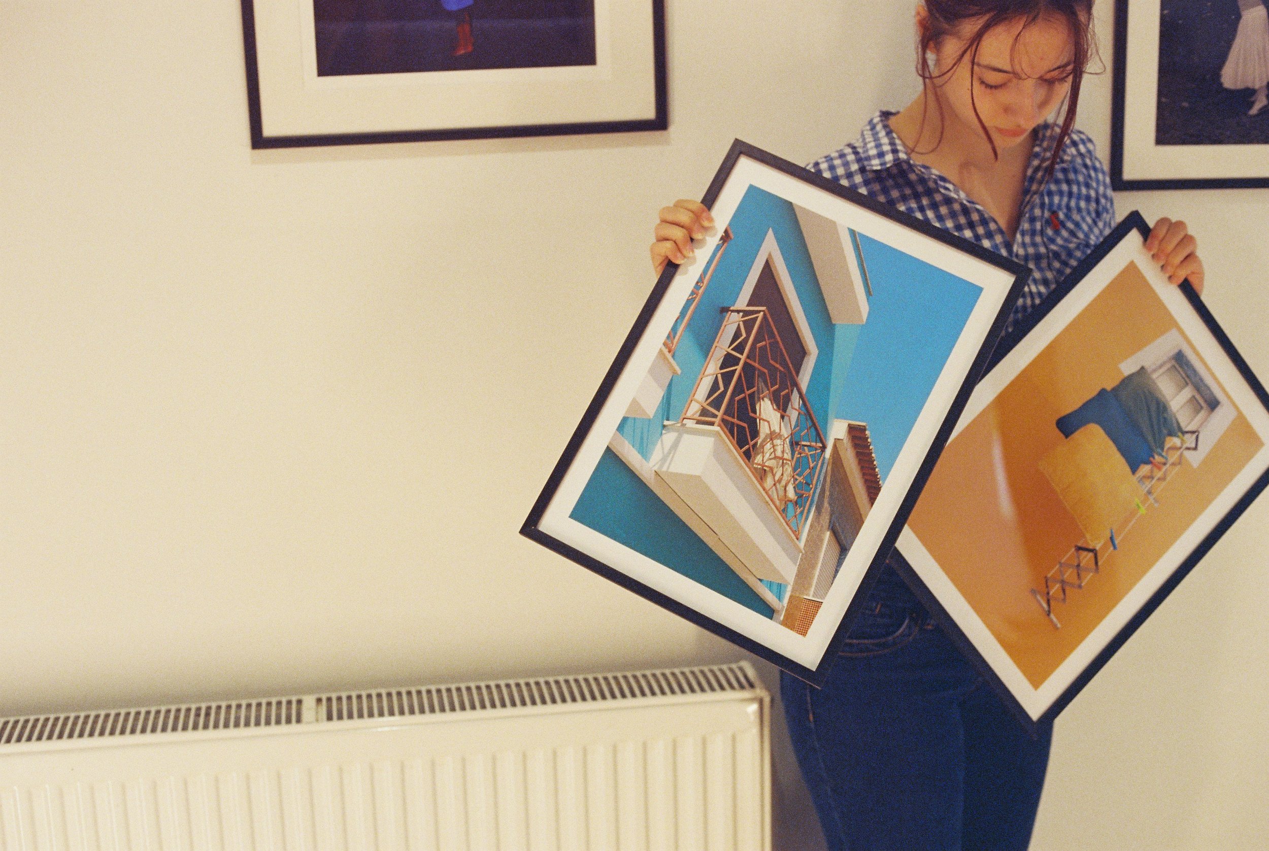 a woman stands holding two framed photos
