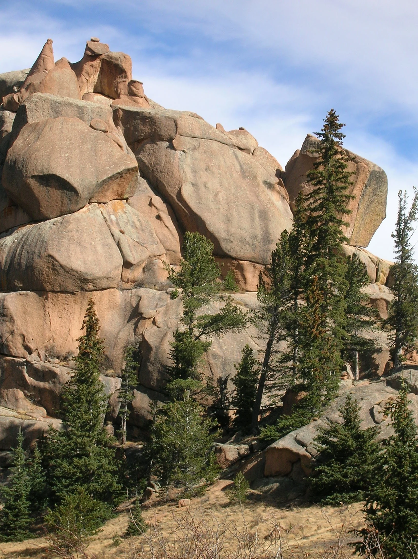Large granite rock formations with trees and sparse vegetation in a mountainous landscape under a partly cloudy sky.