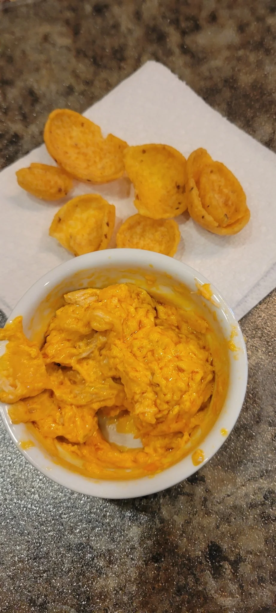 A bowl of scrambled eggs and a few potato chips on a paper towel on a countertop.