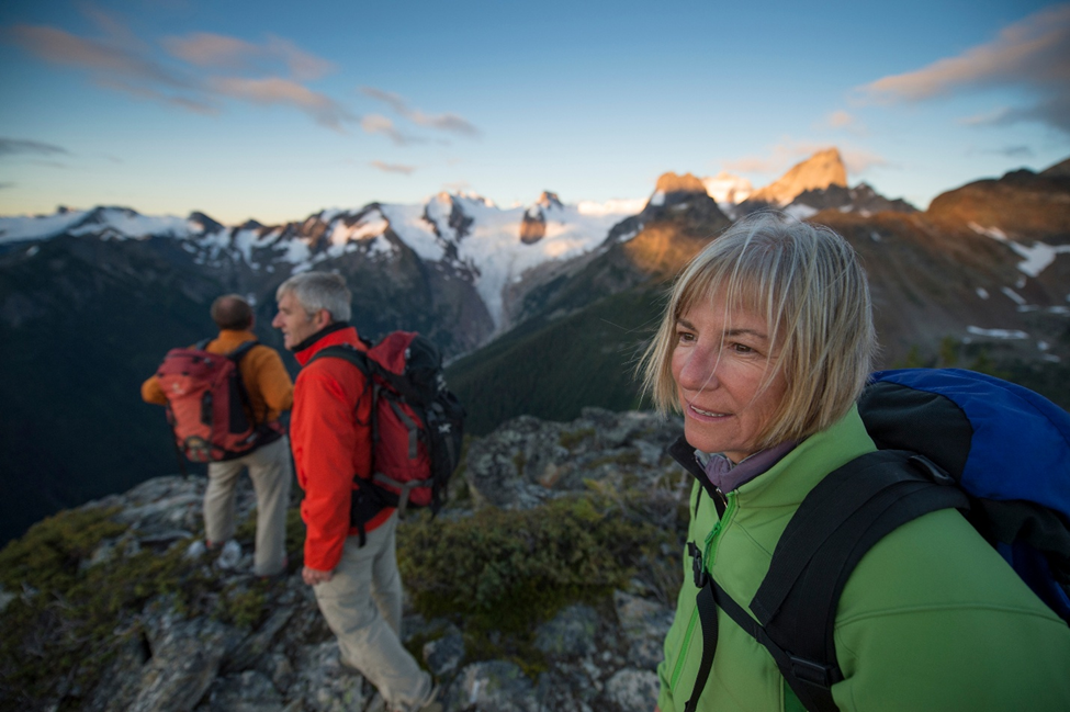 Three hikers on a mountain ridge with snow-capped peaks and a glacier in the background
