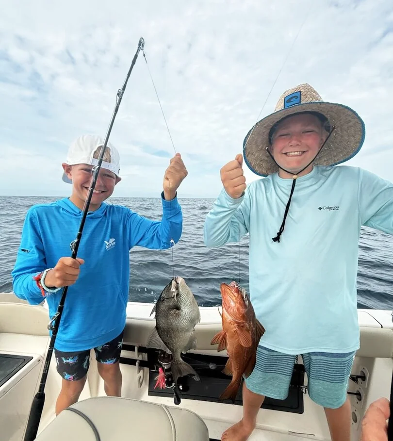 Two young boys hold up a triggerfish and red grouper they caught with Bluewater Charter Along the Gulf Coast