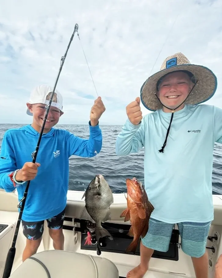 Two young boys hold up a triggerfish and red grouper caught along the Emerald Coast