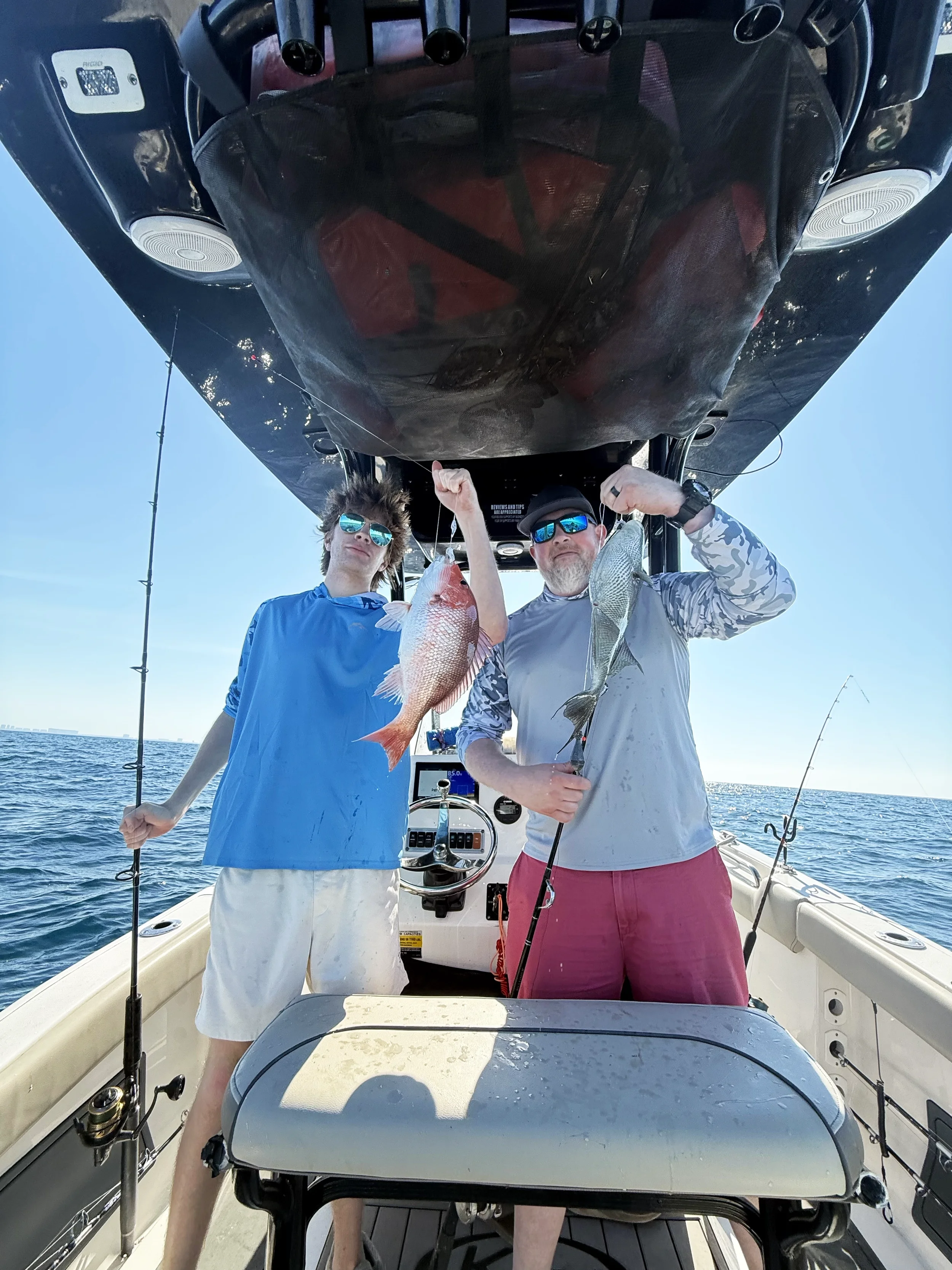A man and his son hold up a red grouper and triggerfish they caught along the Emerald Coast of Florida