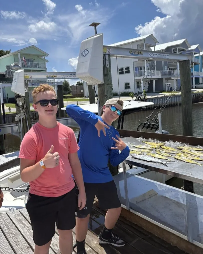 Two young anglers celebrating a successful fishing trip with a table full of freshly caught mahi-mahi at the dock