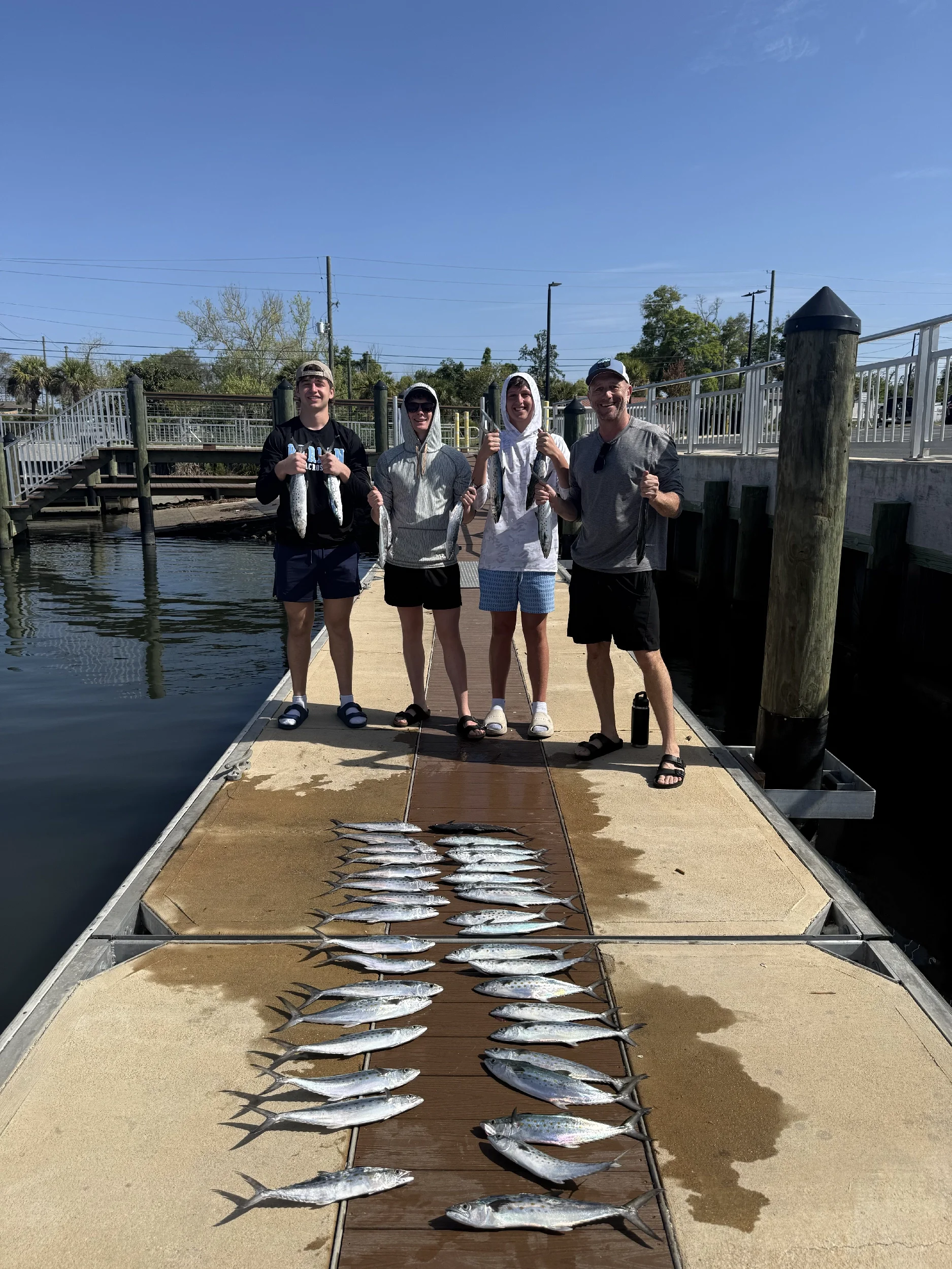 A man and three teens showing off the fish they caught on a dock in the Gulf