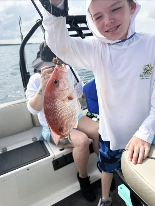 Young angler proudly holding a freshly caught snapper during a family-friendly fishing charter on Florida’s Emerald Coast