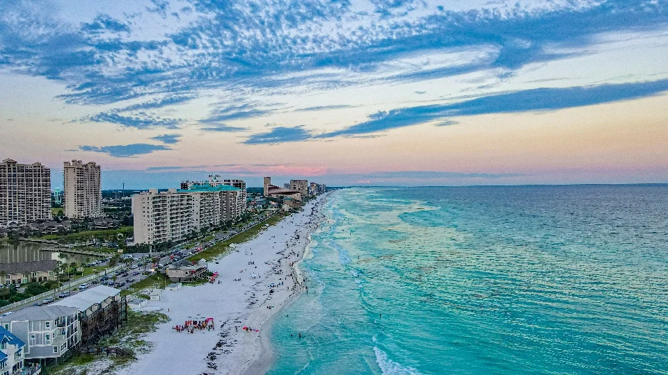 Aerial view of a beachside cityscape during sunset with high-rise buildings, shoreline, and ocean.