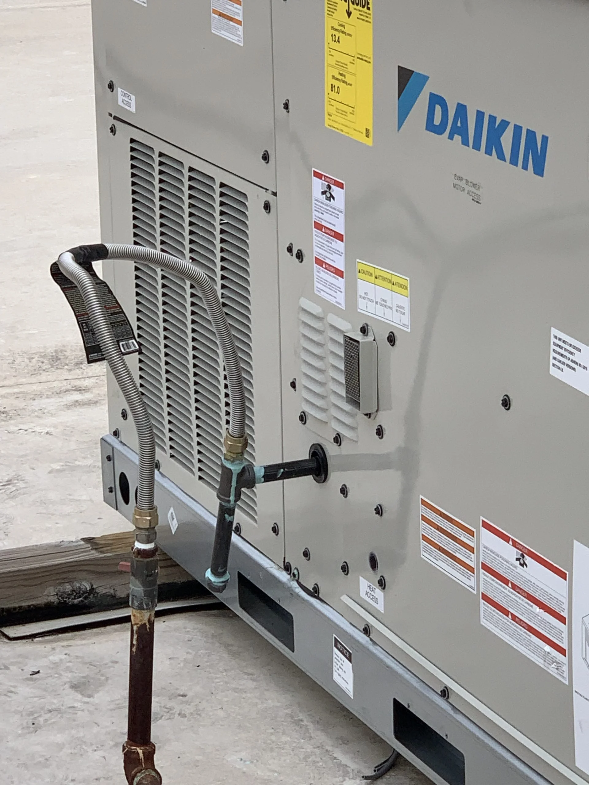 Close-up of a Daikin industrial HVAC unit with connected pipes and various warning labels