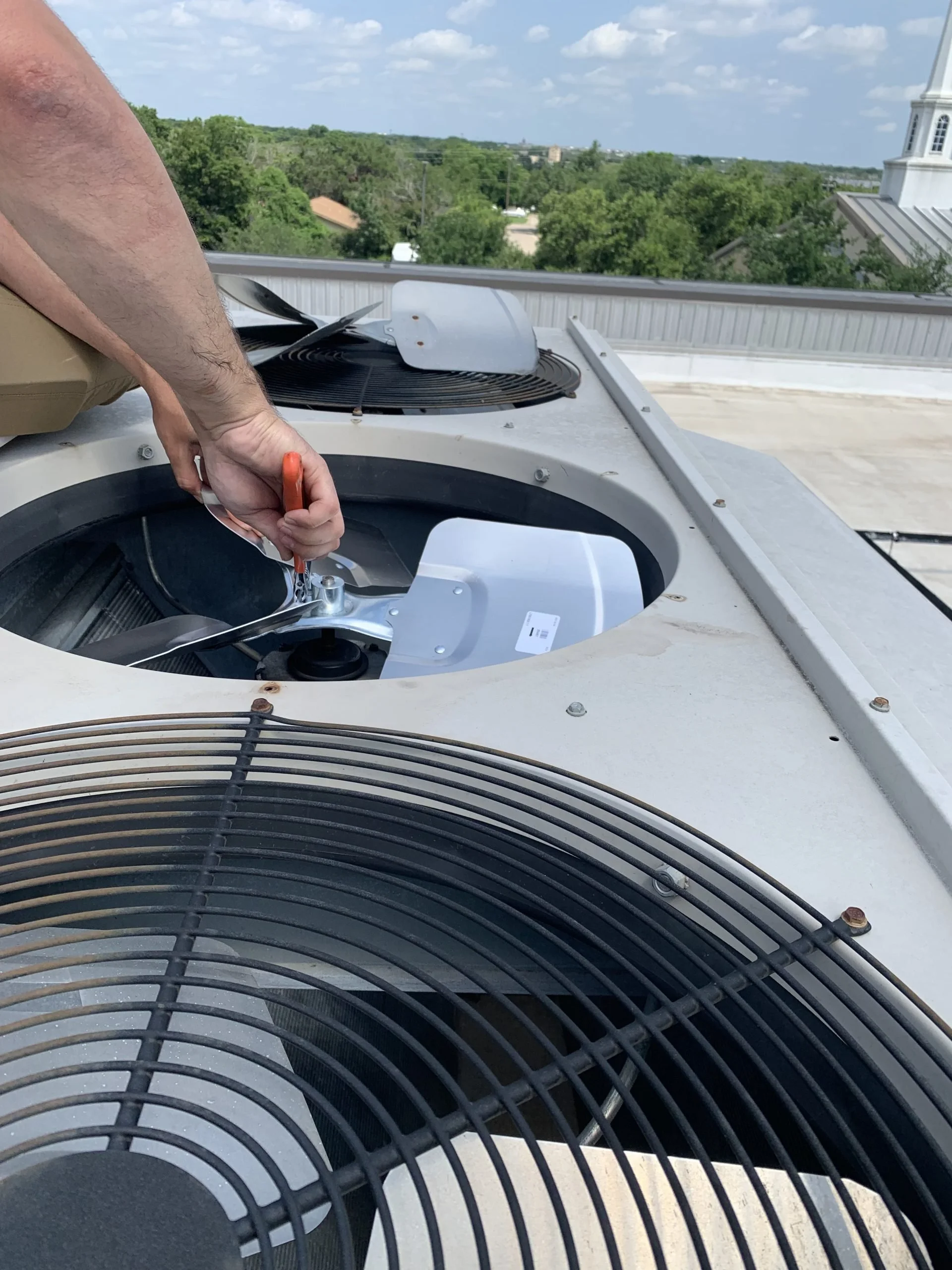 A person working on an air conditioning unit on a rooftop, using a wrench to tighten or loosen a bolt.