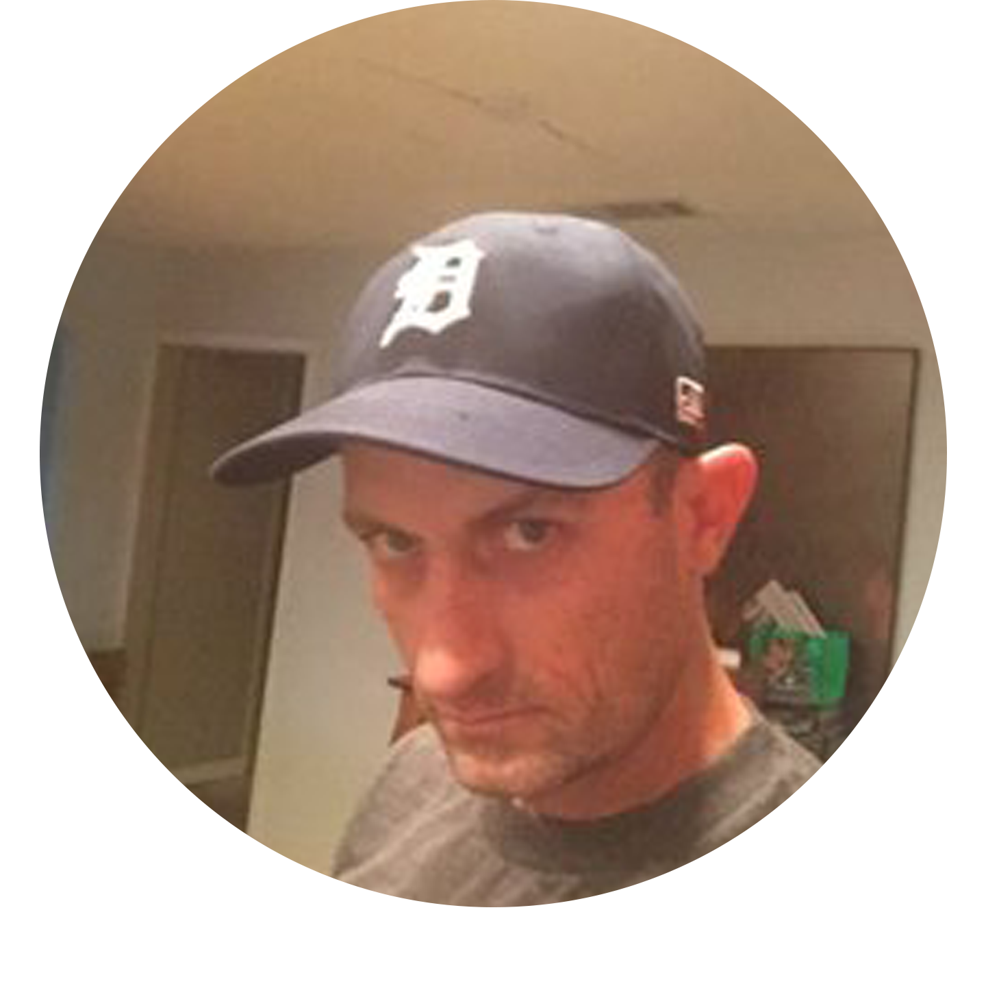 A man wearing a dark baseball cap with a white letter 'D' on it, looking slightly to the side with a serious expression.