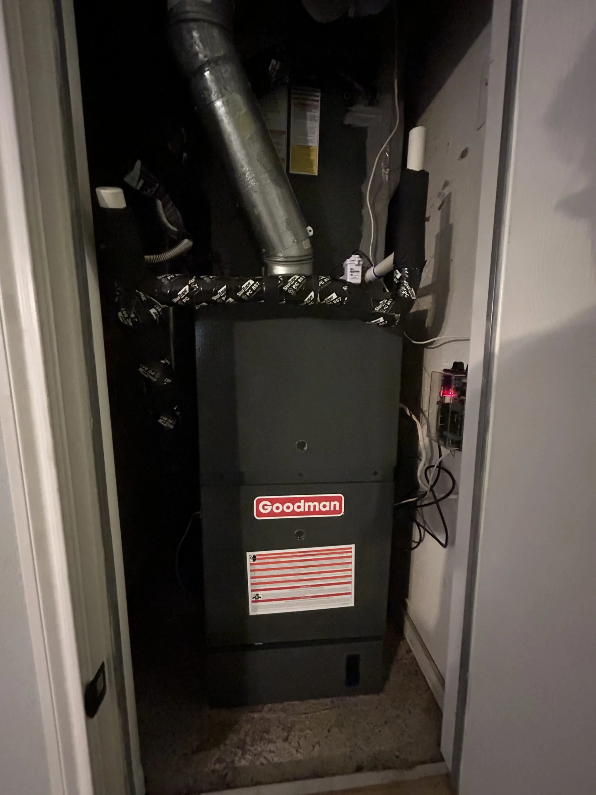 Furnace in a closet with a silver duct and wires visible.