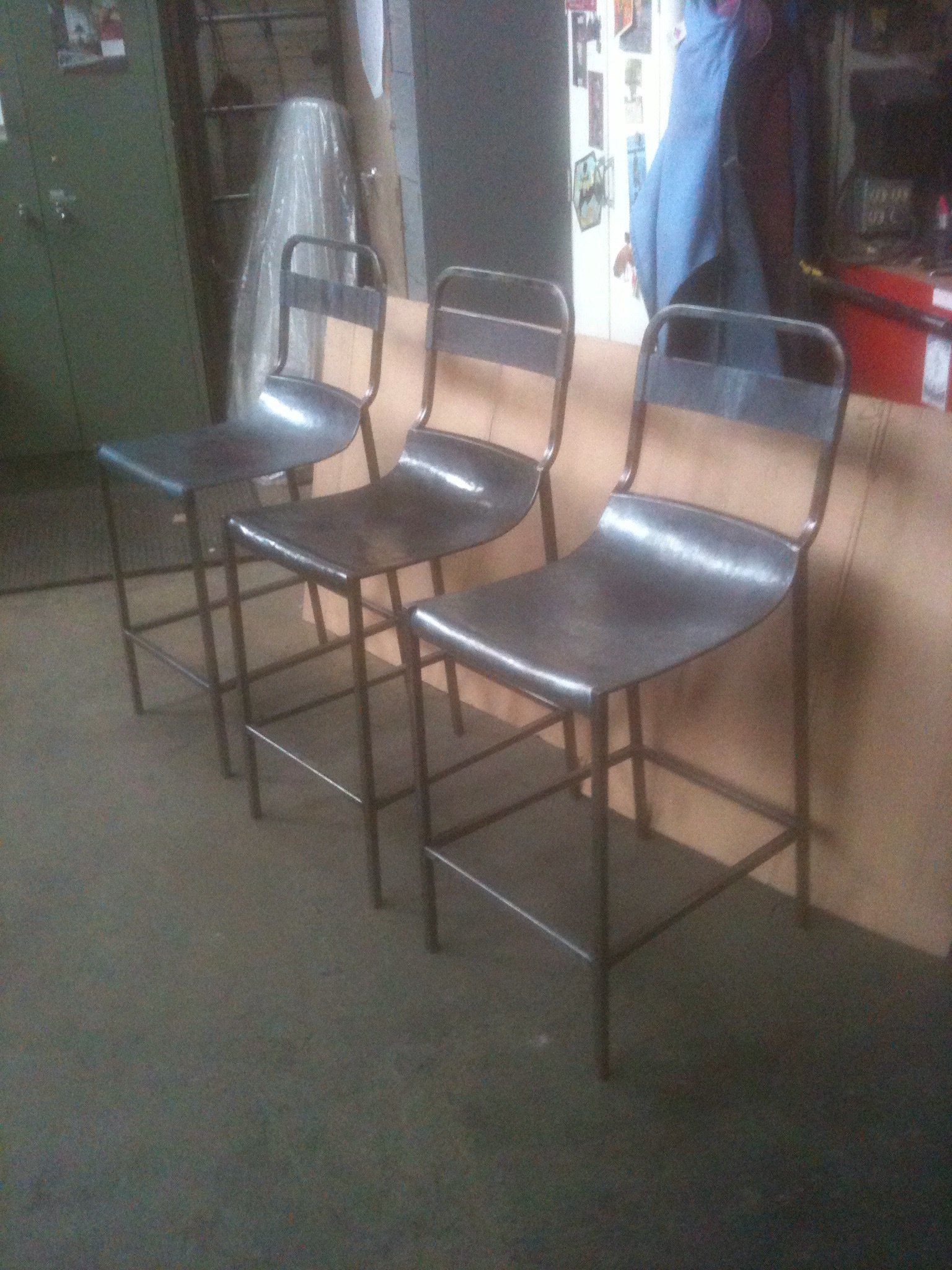 Three black metal barstools with backrests.