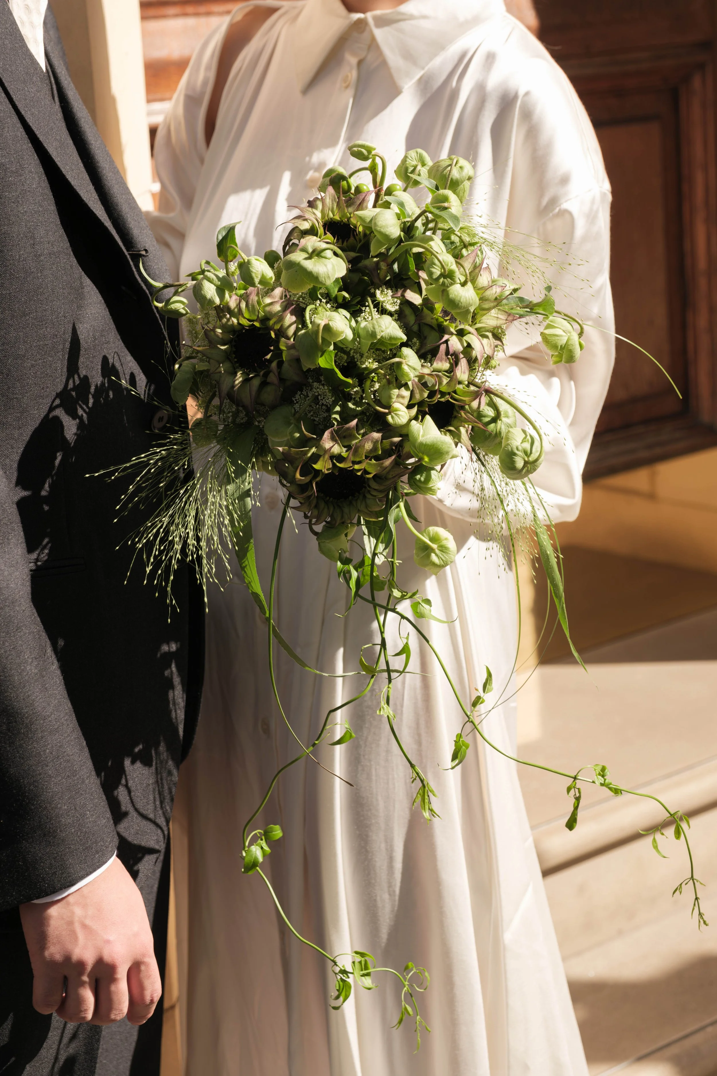 A bride holding a cascading bouquet of green flowers and foliage during a wedding ceremony.