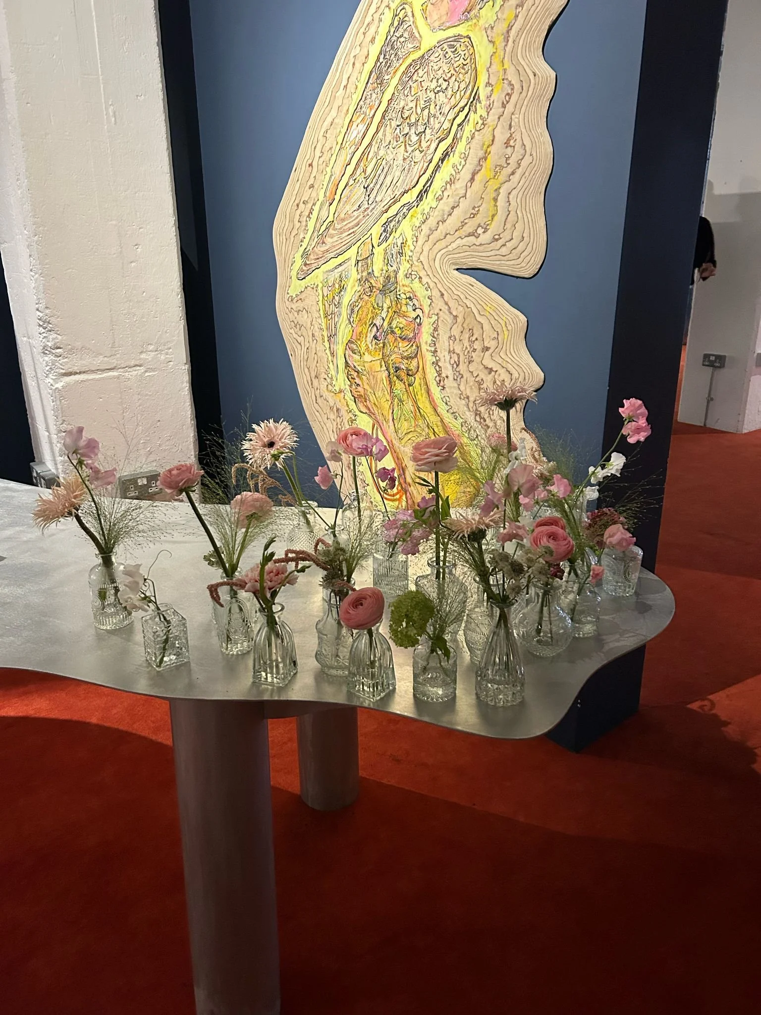 A table with pink and white flowers in small glass vases in front of a large abstract artwork on the wall.