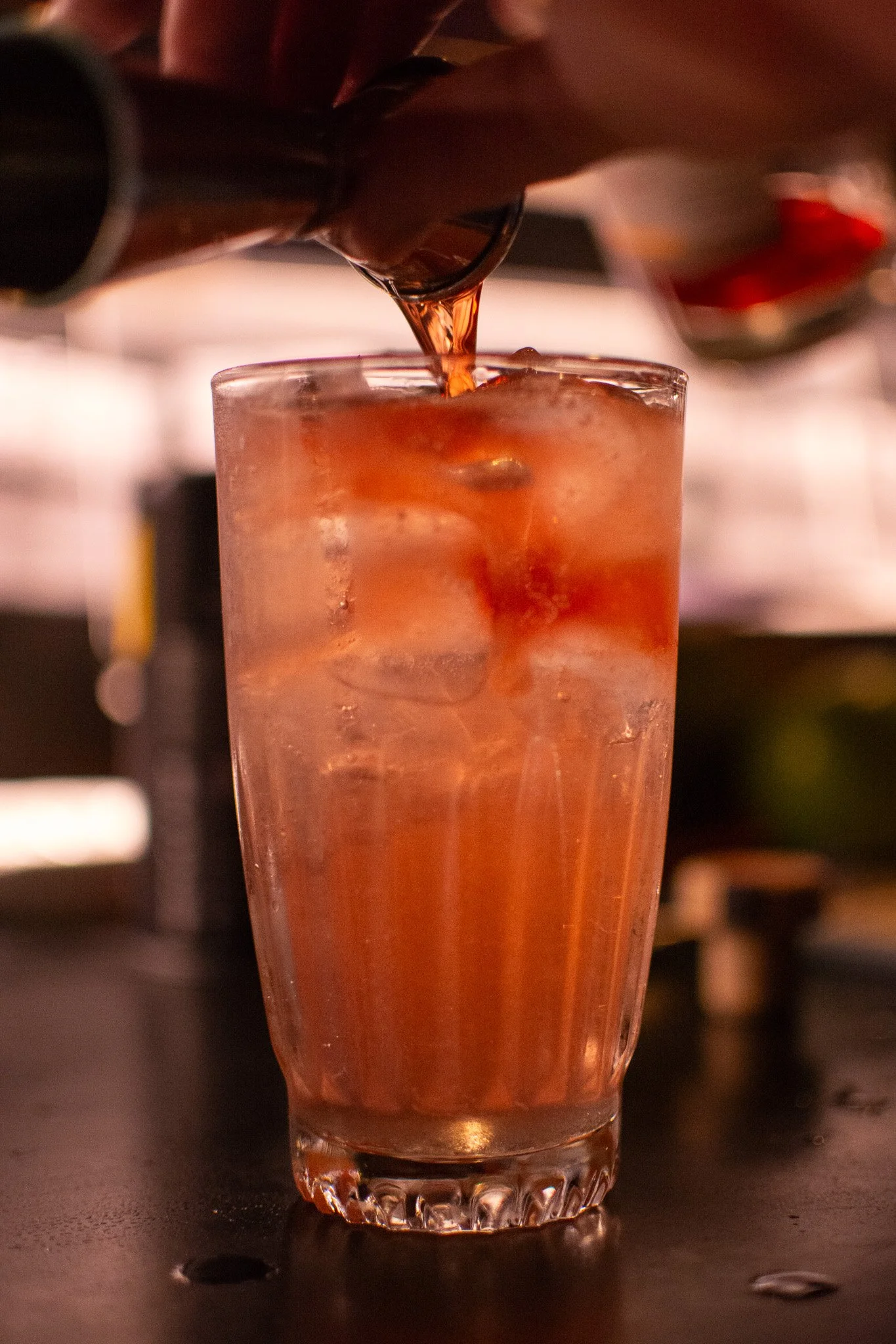 cocktail in tall glass, gin being poured into glass with ice and cocktail in glass