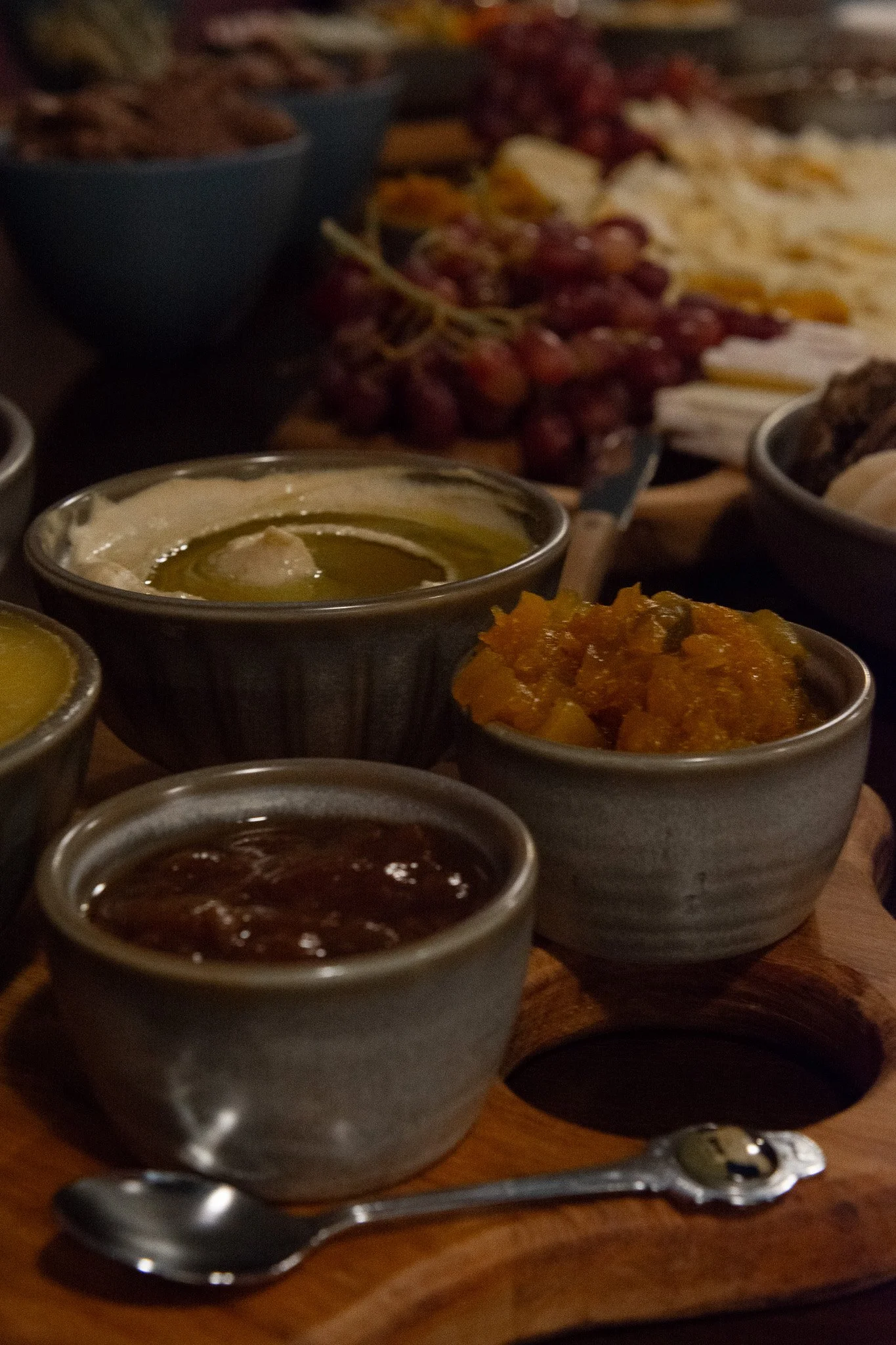 feijoa chutney in ceramic ramekin, pineapple jalapeno lime chutney in ceramic ramekin, homemade hummus with new zealand olive oil in ceramic bowl, fresh red grapes, brie cheese on wooden board, vegan pate