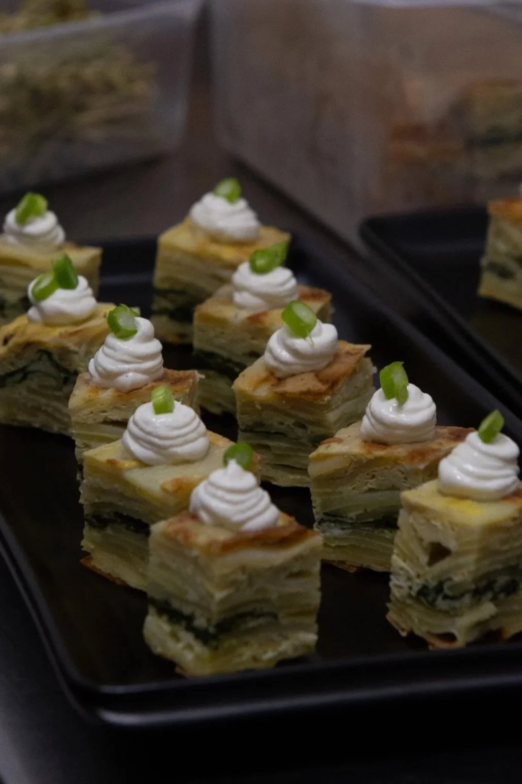 canape of spanish frittata make with egg, potato, onion and spinach with feta yoghurt sauce and green onion garnish on black platter