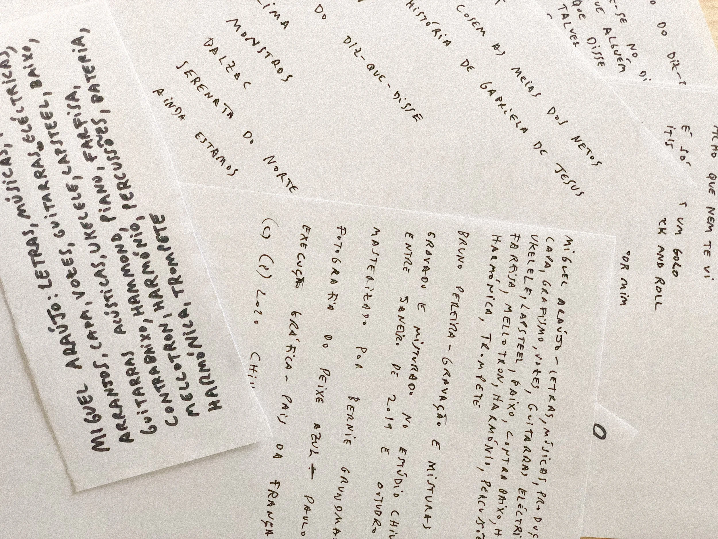 Pedaços de papel com textos manuscritos em português, presos na parede com fita transparente.