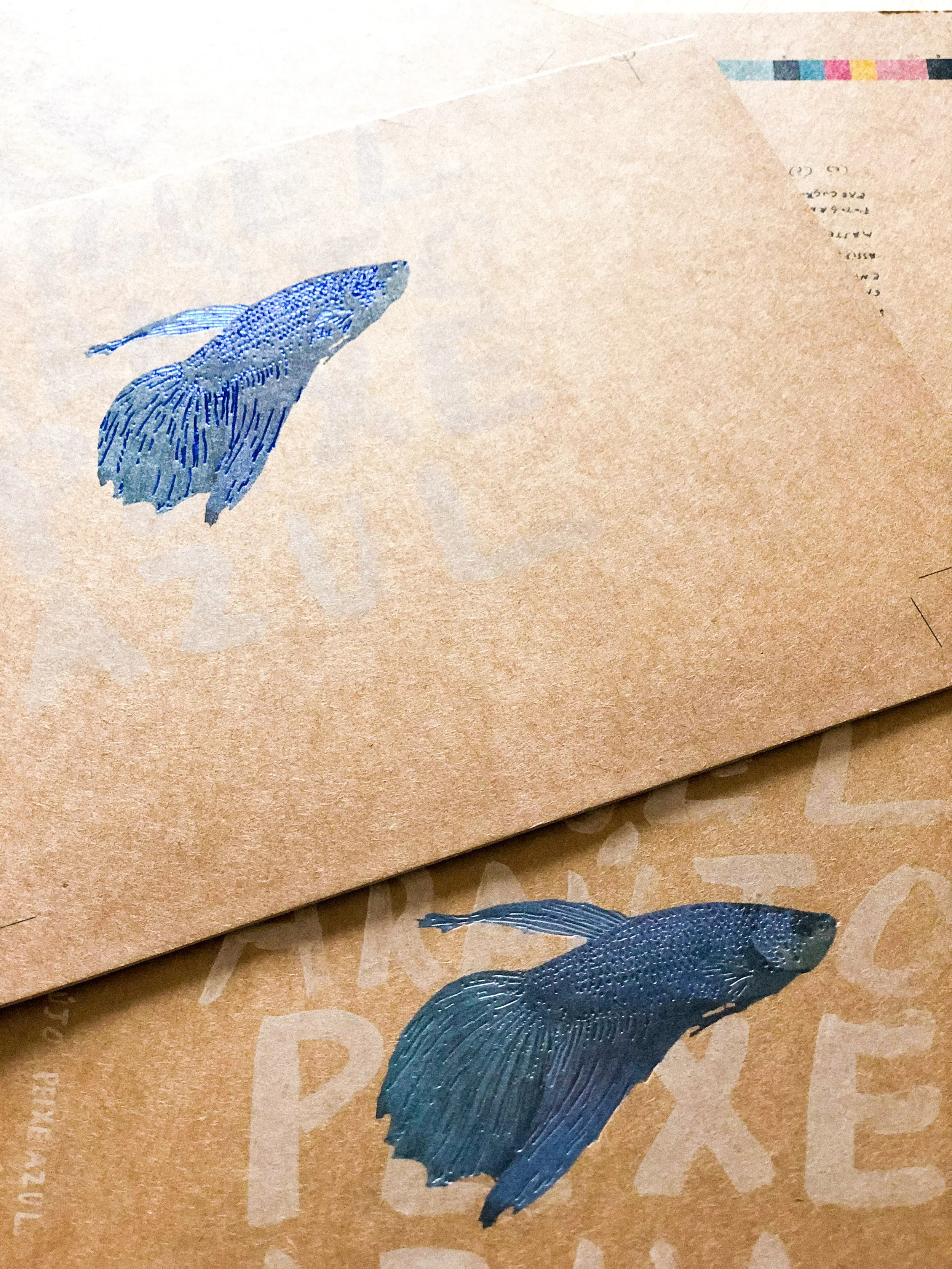 Duas etiquetas com ilustrações de peixes de cor azul, uma sobre papel cartão marrom, outra sobre papel pardo.
