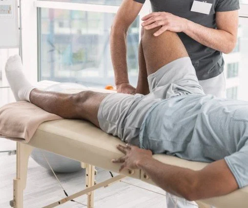 Physical therapist examining a patient's leg on a treatment table in a clinical setting.