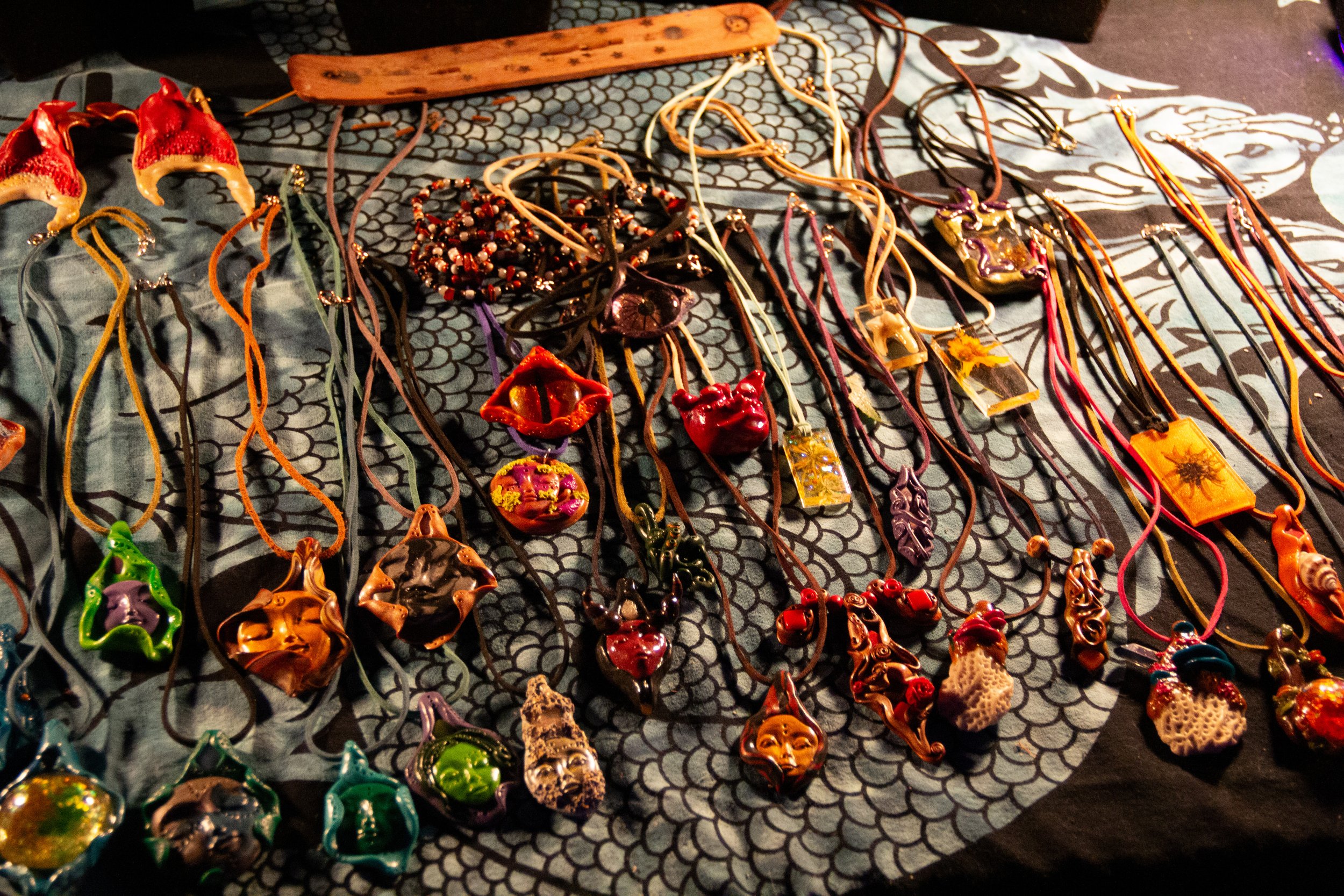 Collection of colorful handmade jewelry, including necklaces and pendants, arranged on a decorative fabric surface at a market stall.