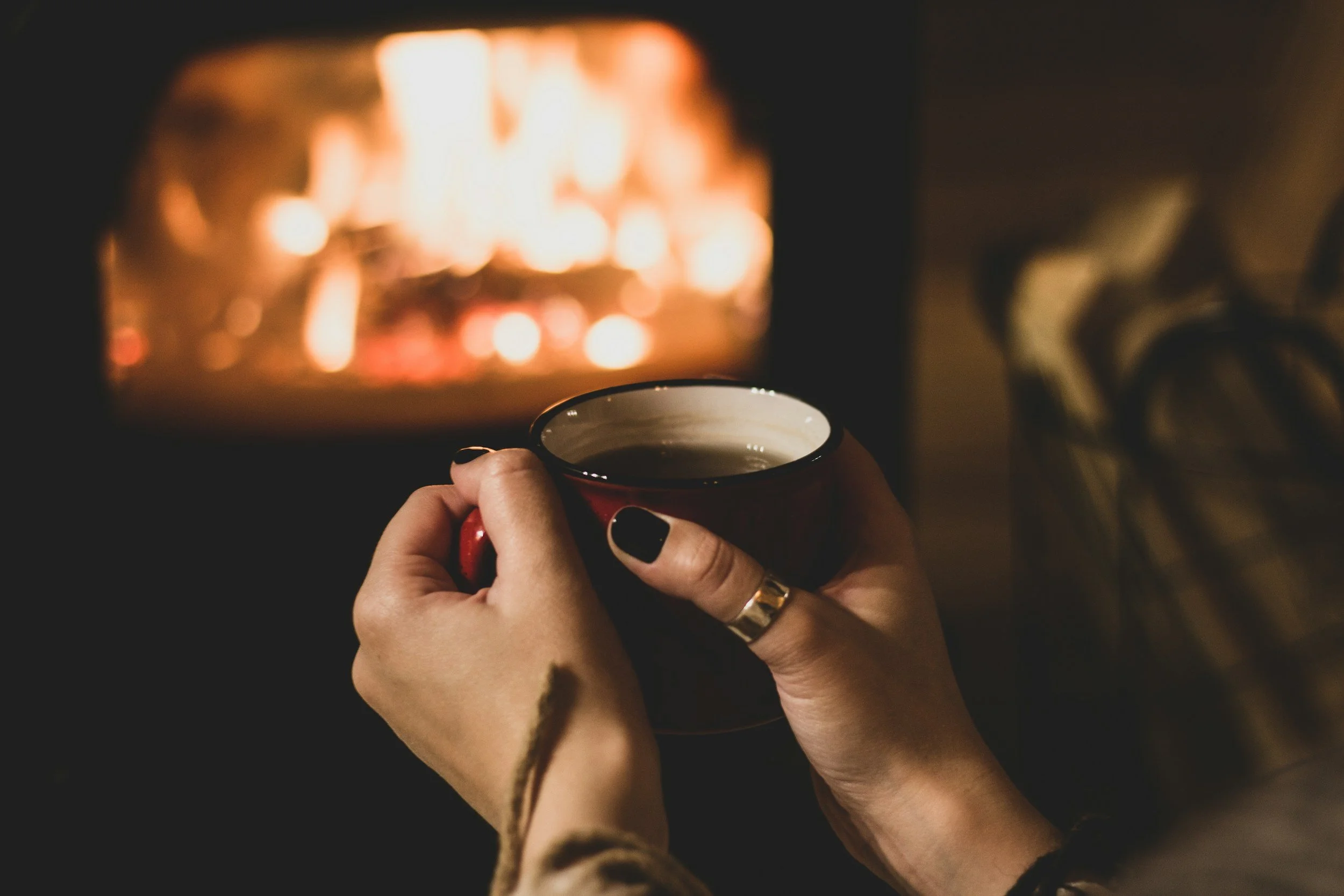 Person holding a ceramic mug indoors at night with a fireplace in the background.