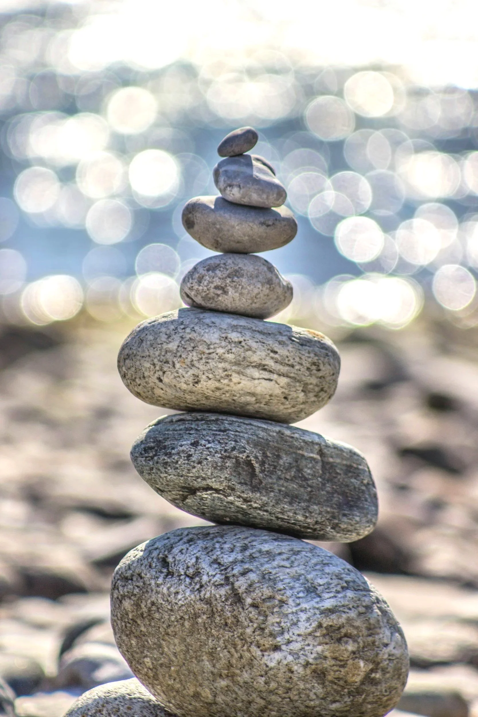 Stacked rocks on a beach with blurred water and sunlight in the background.