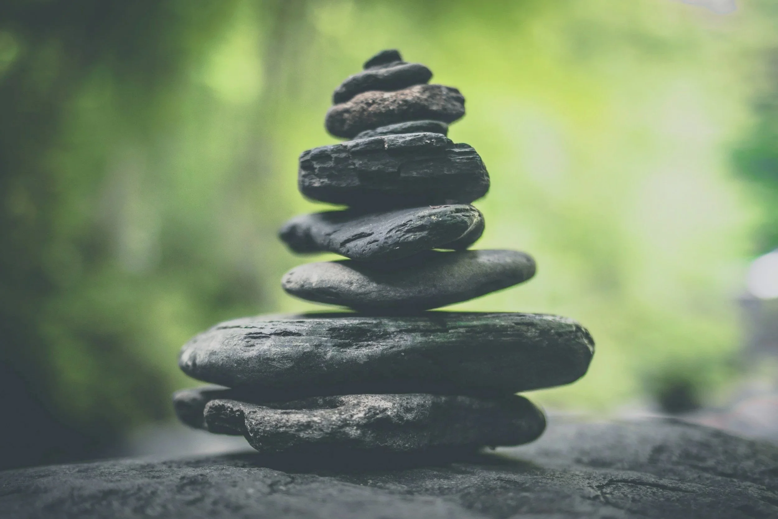 Stack of flat, dark rocks balanced on top of each other outdoors with a blurred green background.