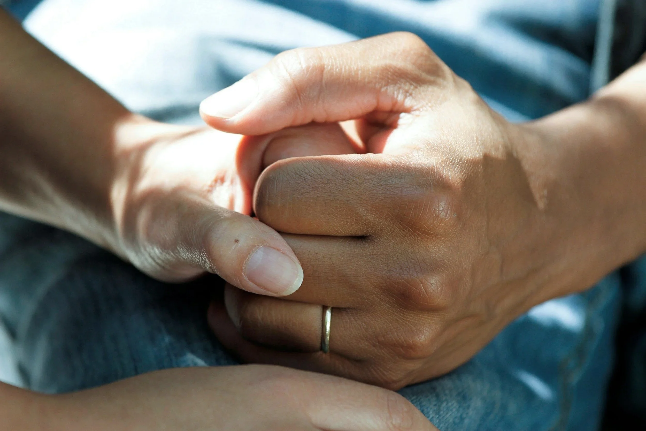 Close-up of two hands clasped together, one hand on top of the other, with a thin ring on the finger of the hand on top.