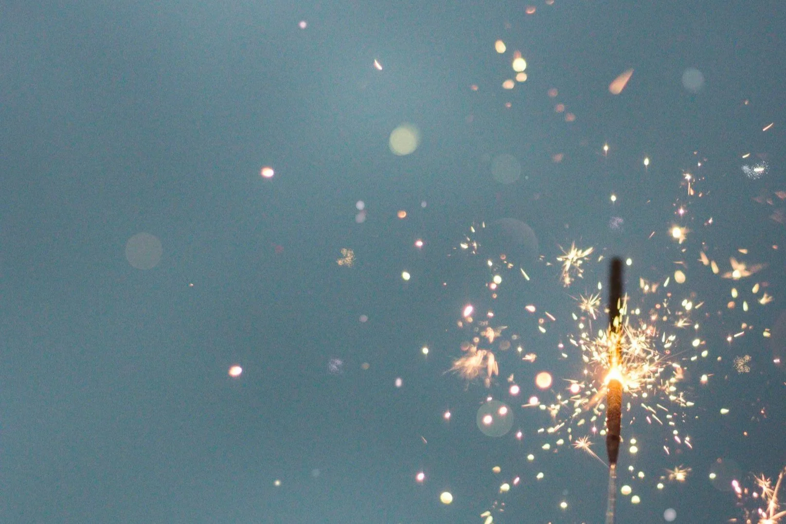 Firework sparkler emitting bright sparks against a blue sky.