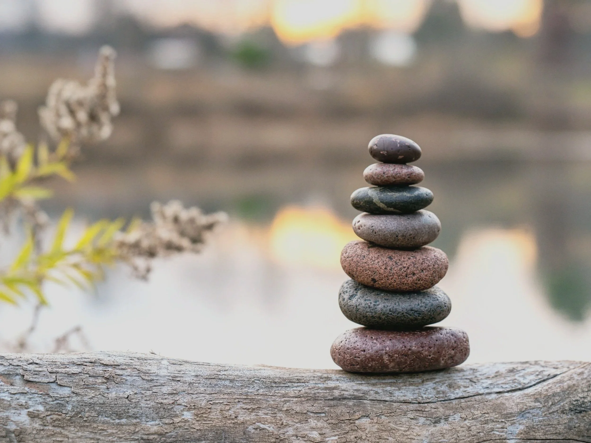 A stack of seven smooth, rounded stones balanced on top of a weathered wooden surface outdoors during sunset.