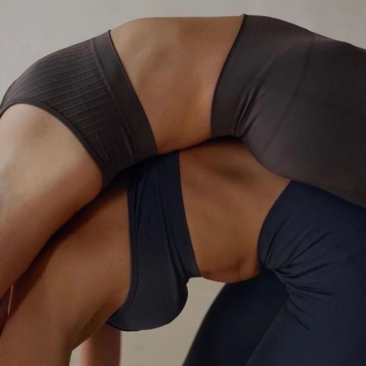 Two women in athletic clothing practicing yoga or stretching indoors.