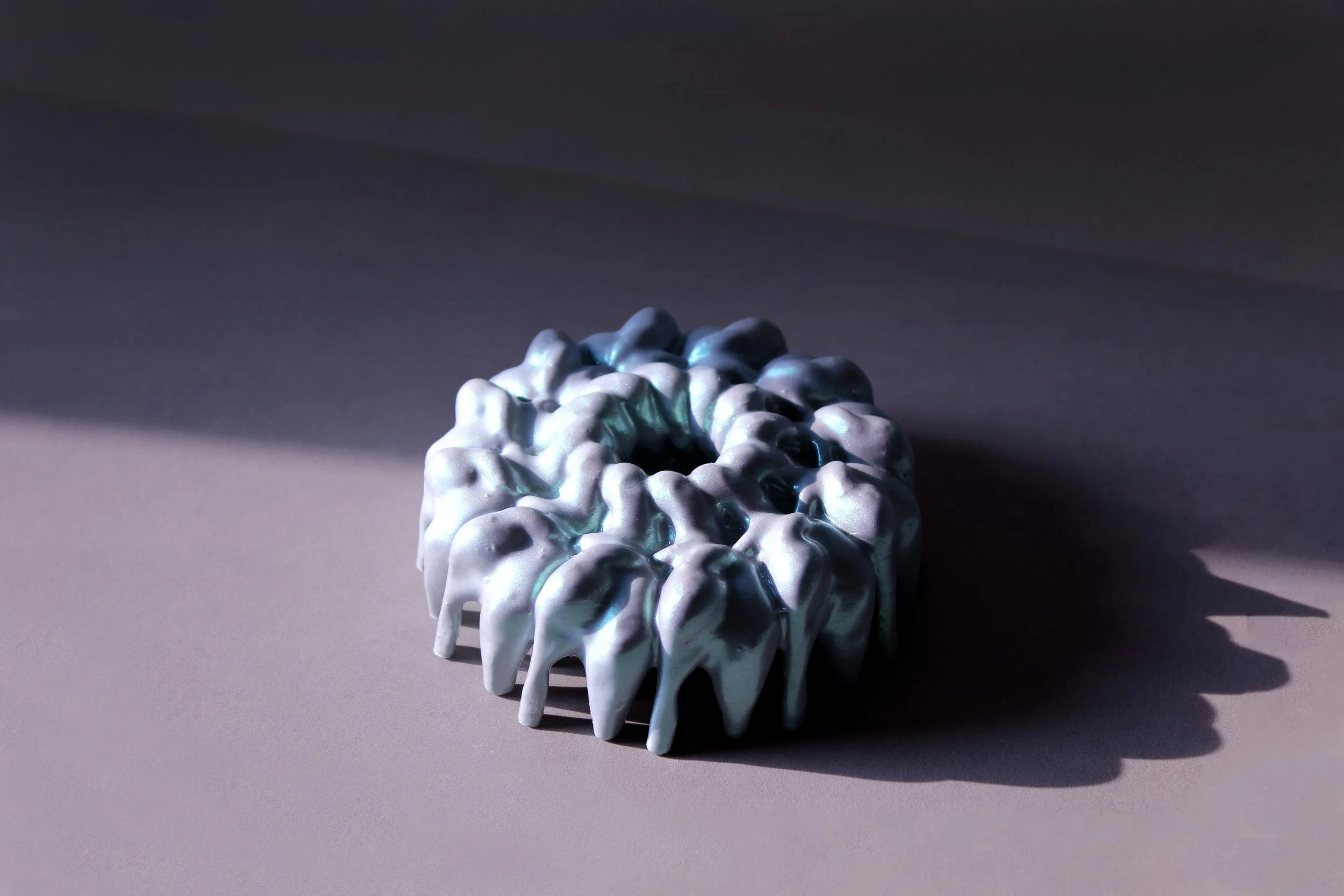 Circular iridescent object composed of interconnected, tooth-like forms forming a ring structure, part of the Pet Objects Multiple series