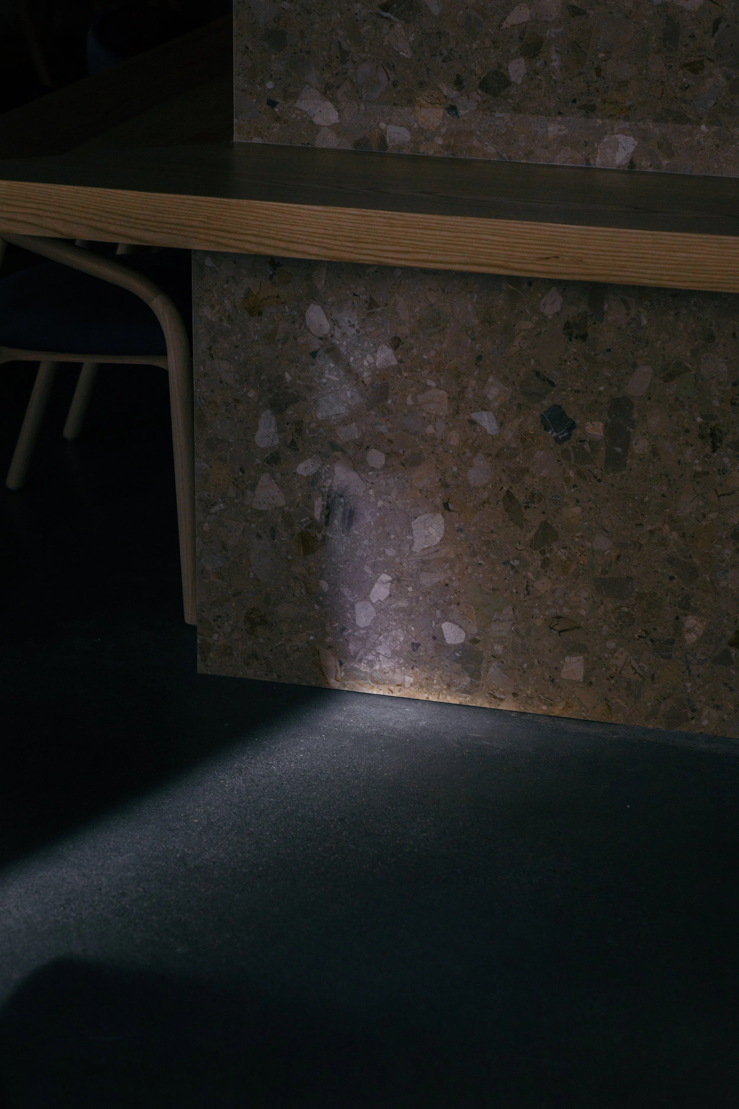 Detail of daylight washing across stone surface and concrete floor