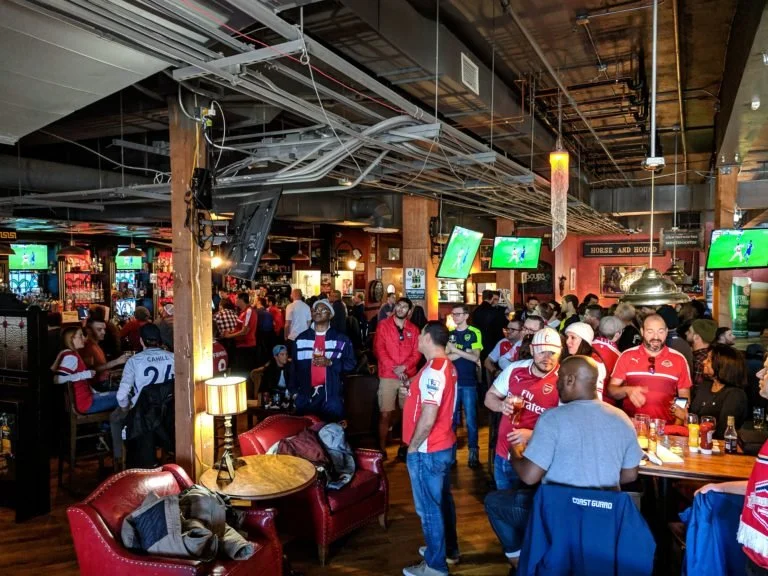 Crowded sports bar with people in red jerseys watching soccer on TV