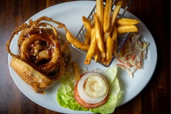 Plate with fried onion rings, French fries, coleslaw, and a burger with lettuce, tomato, onion, and a bun.