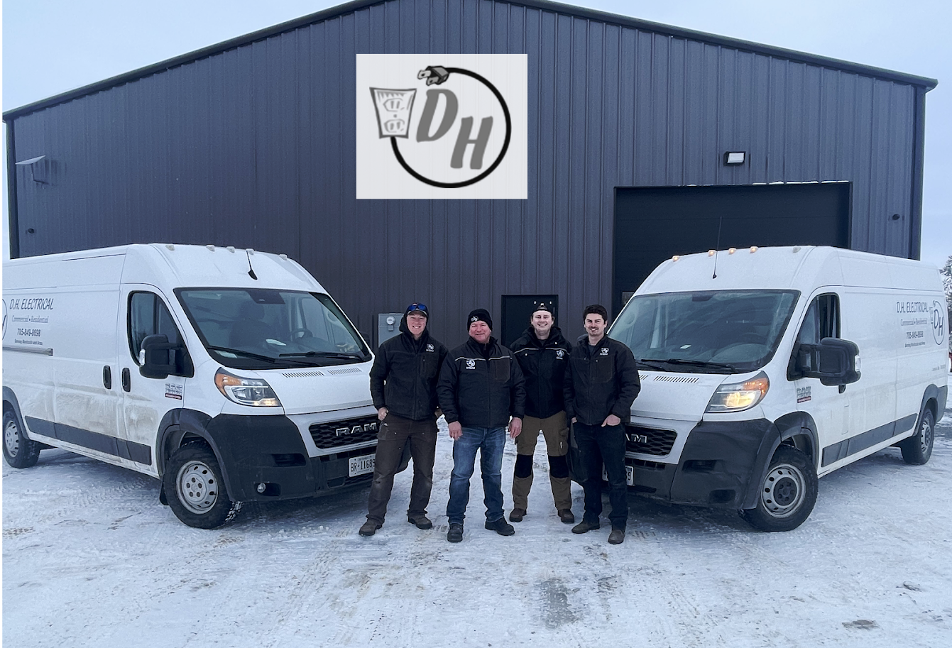 Four men standing in front of a huge shop with the DH Electrical Logo on the front of it and two white utility vans on the side