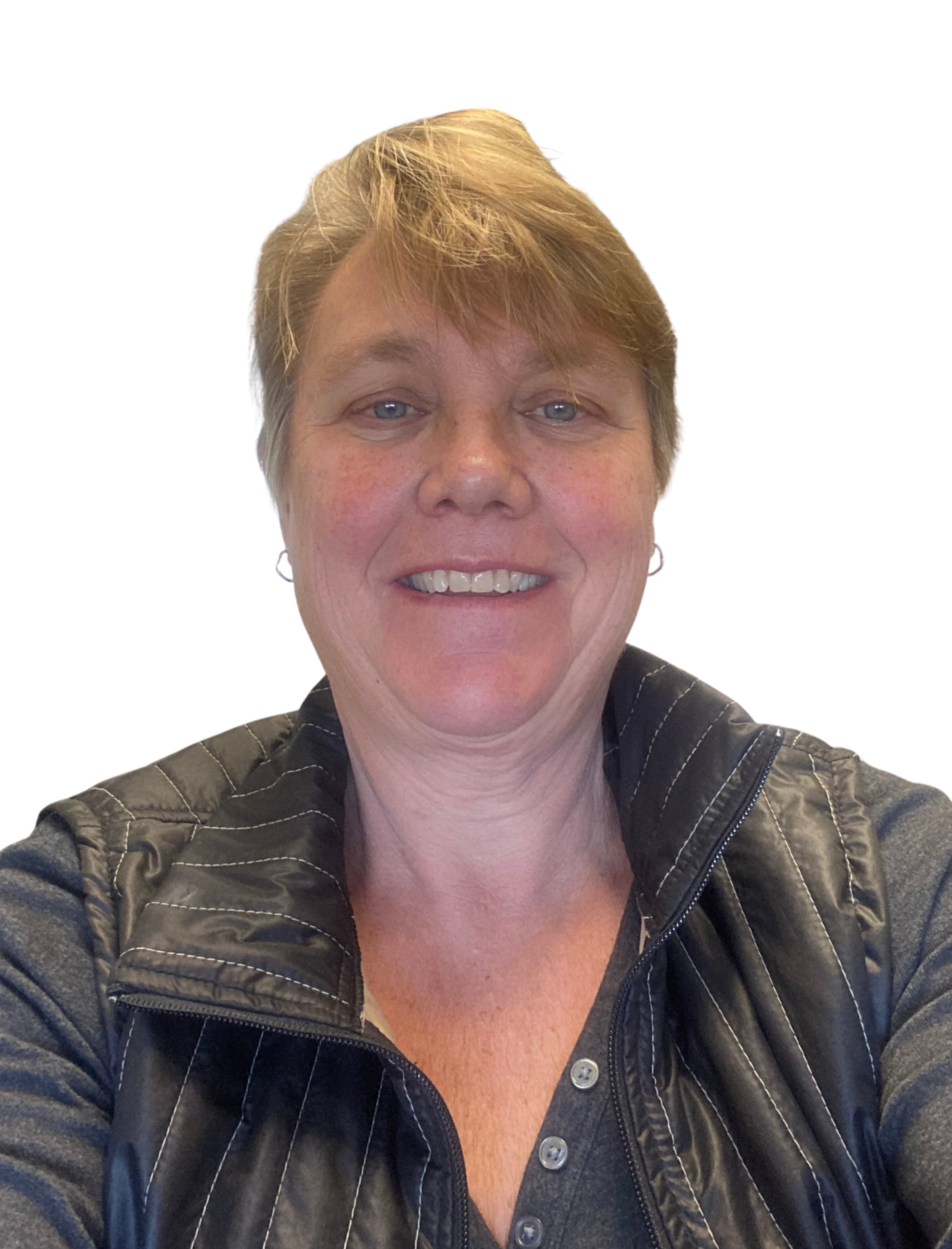 Selfie of a smiling woman with short light brown hair, wearing a dark vest over a shirt, against a white background.