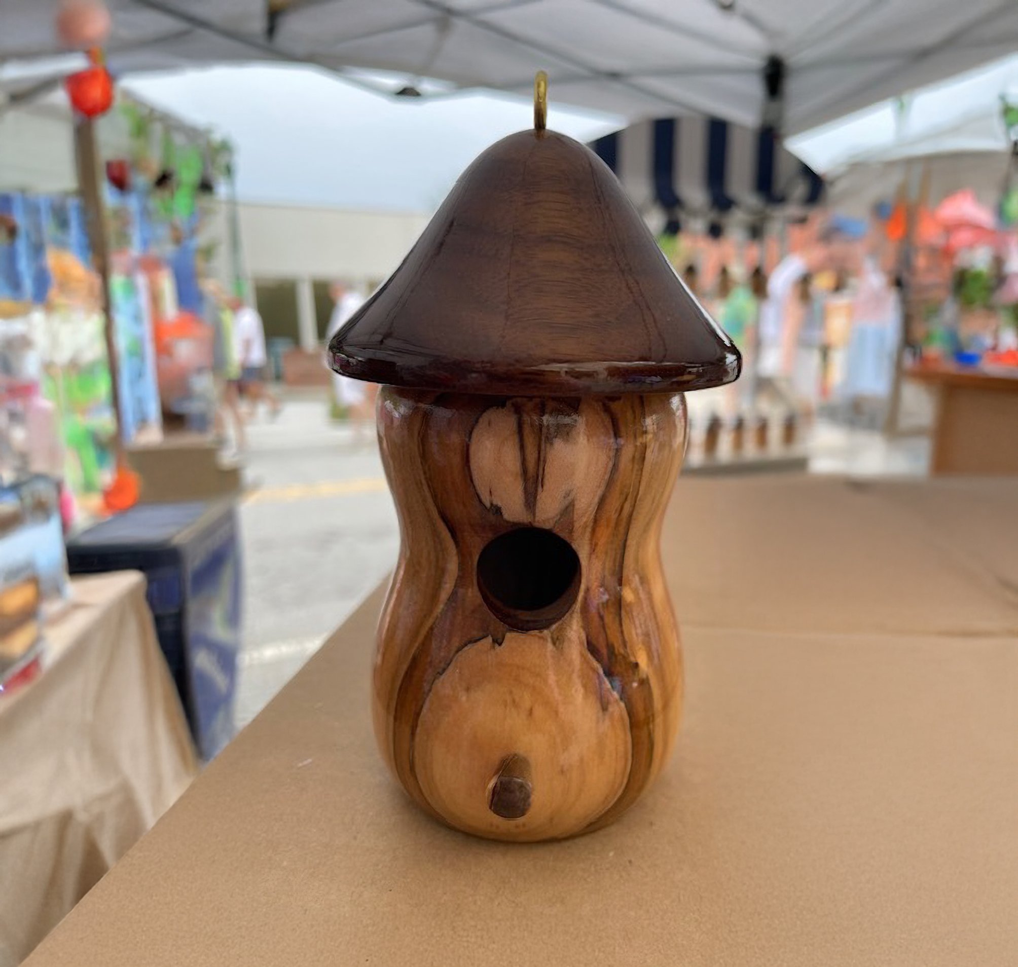 Wooden gourd-shaped birdhouse with dark brown roof on display at a market stall.