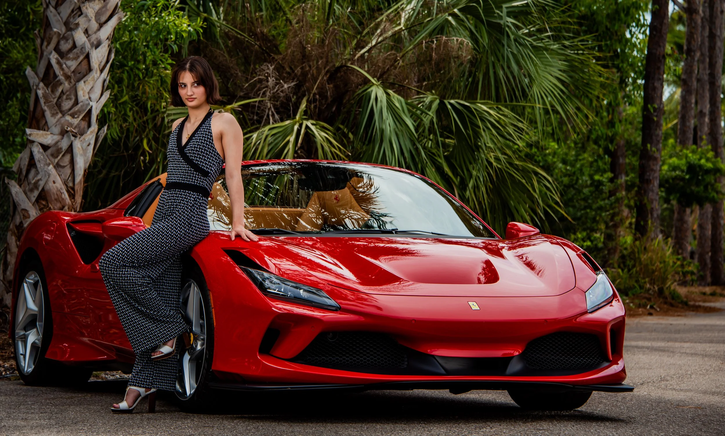Portrait of a dark-haired female model leaning against a red Ferrari.