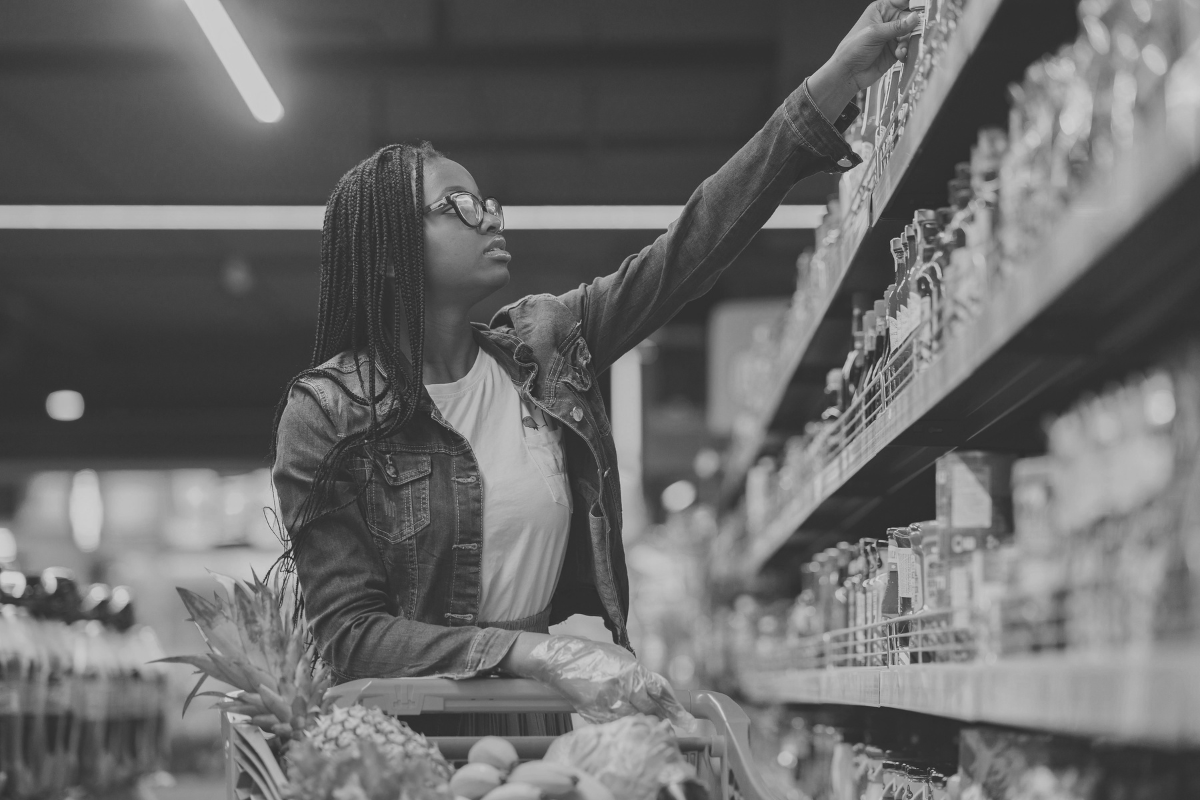 Woman shopping in a grocery store aisle, reaching for products on a shelf, representing consumer behavior and PR impact in the food and beverage industry.