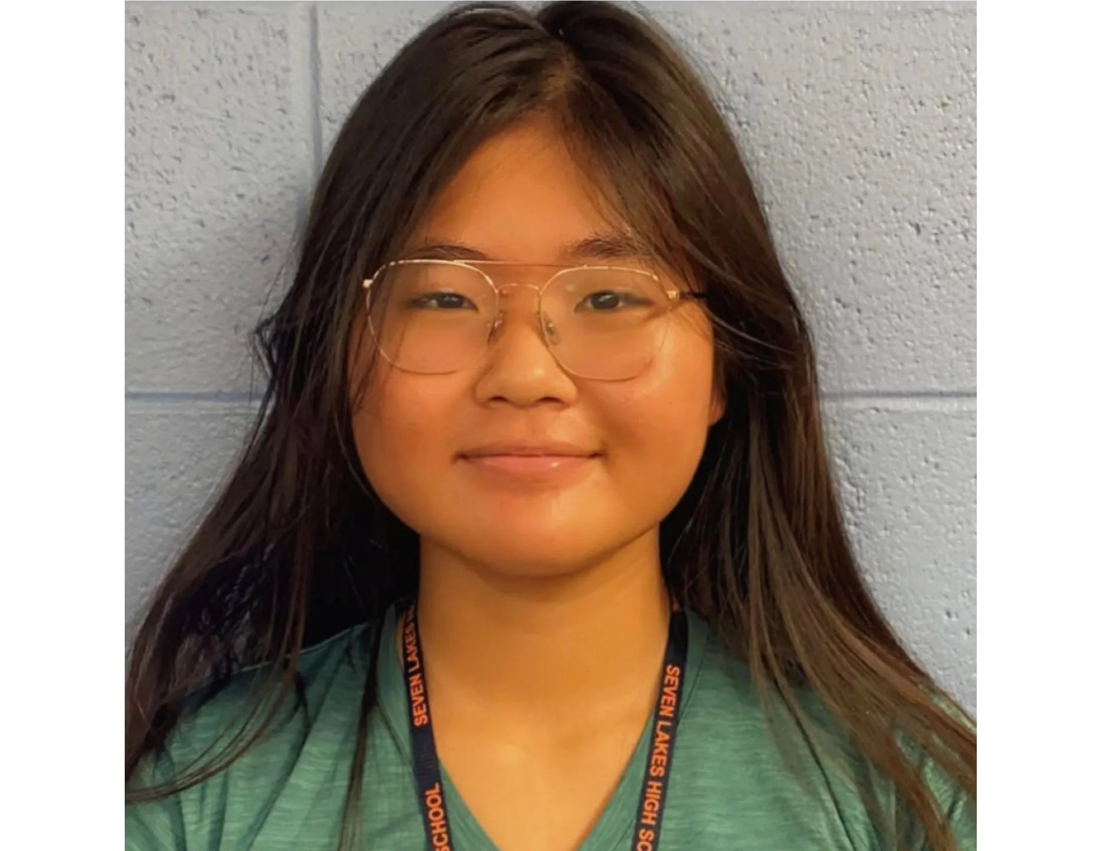 Portrait of a person wearing glasses and a lanyard in front of a light blue wall.