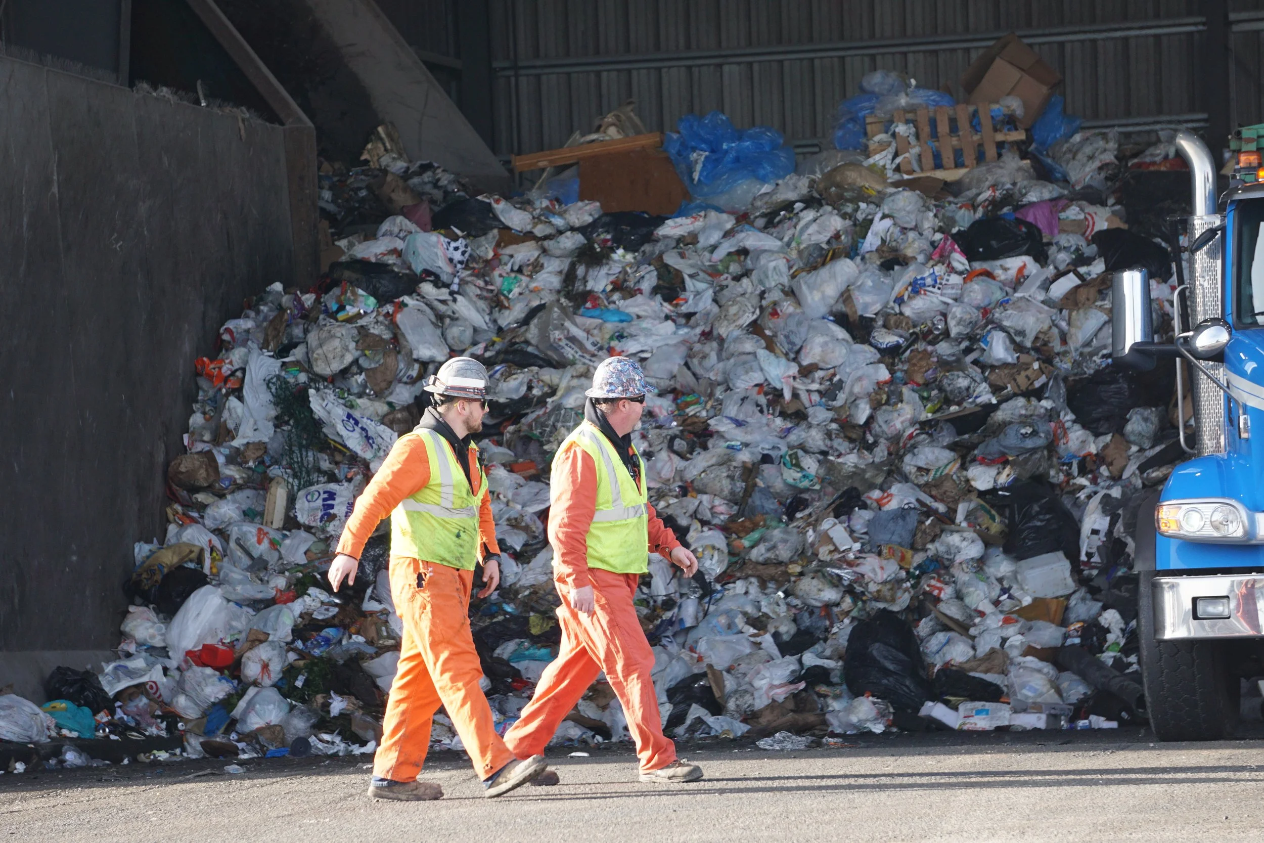  Two workers walk outside the main garbage tipping floor at Recycling &amp; Disposal Services in Ferndale, Wash., on Feb. 6, 2026. These staff typically help guide customers to the proper spot to unload trash or mixed recycled waste. Due to increased