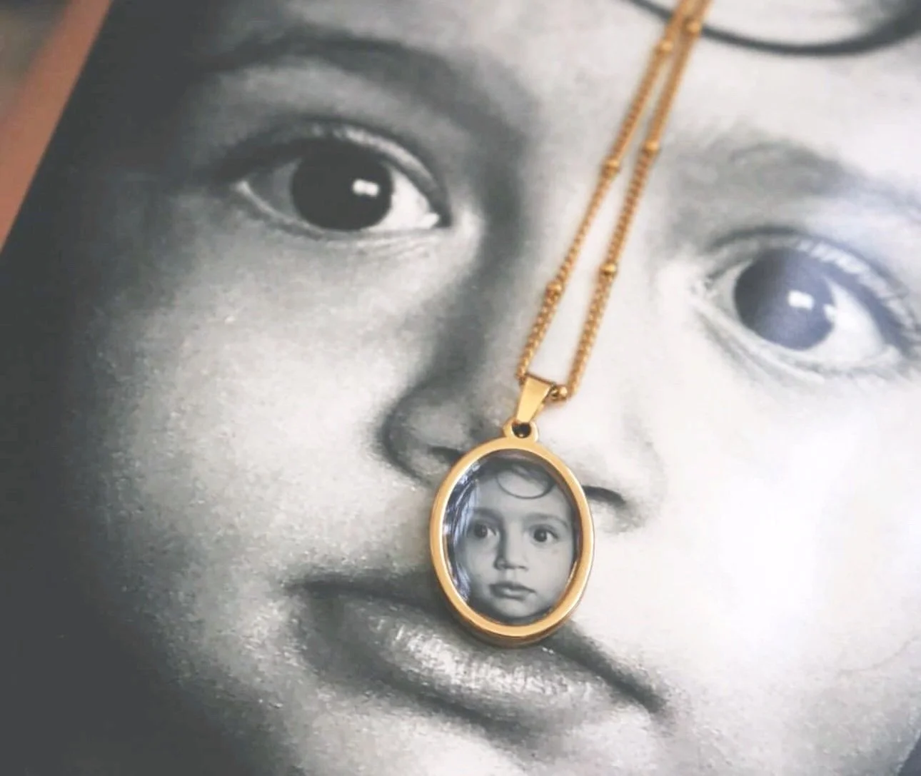 Medallón dorado con la foto de un niño, sobre una fotografía en blanco y negro del mismo niño.
